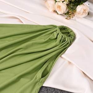 Detail of green summer dress featuring elastic waist and side seam pocket on satin background