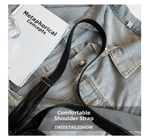 Detail of black leather bag strap with dark gray metal adjustment buckle on denim fabric