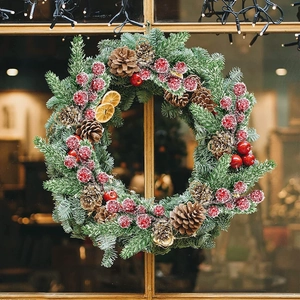 Detail of Christmas wreath with pine cones, red berries, and dried orange on wood window