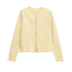 Detail of light yellow knit cardigan featuring ruffled cuffs and hem with button closure
