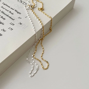 Minimalist silver and gold square chain necklaces styled on an open book background