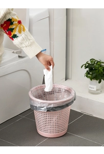 Pink hollow mesh trash can with wide opening and gray liner in bathroom setting