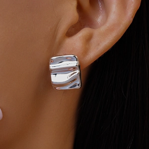 Macro shot of silver liquid metal style square stud earrings with wavy texture