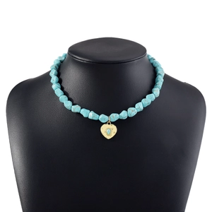 Detail of bohemian turquoise beaded necklace with golden heart pendant on black display
