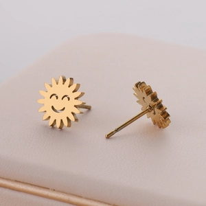 Macro view of gold sun face stud earrings on pink textured jewelry box surface