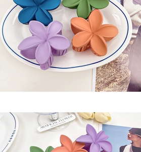 Close-up of matte plumeria hair claws in navy, green, purple and orange on a ceramic plate