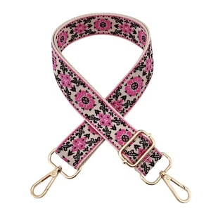 Detail of floral embroidery on wide woven bag strap with golden metal swivel hooks