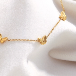 Halskette aus 18K vergoldetem Edelstahl mit drei 3D-Schmetterlingen auf weißem Stoff