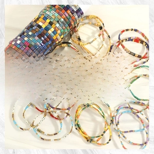 Detail of bohemian Tila beads bracelets with colorful enamel tile patterns and gold accents