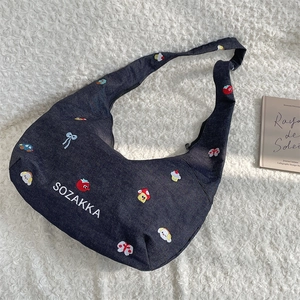 Close-up of embroidered denim crescent bag with colorful strawberry and mushroom icons