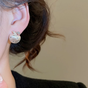 Detail of silver apple-shaped stud earring with star engraving on a model's ear