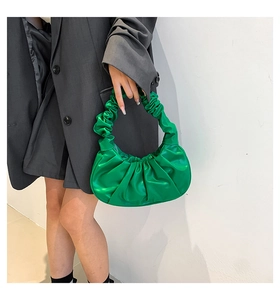 Detail shot of bright green pleated cloud bag held by a model in grey suit