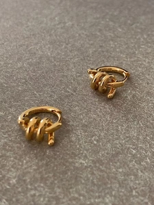Detailed close-up of golden S925 sterling silver twisted hoop earrings on grey background