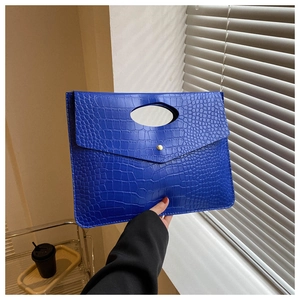 Close-up of blue crocodile pattern leather clutch bag with gold button and hand-held handle