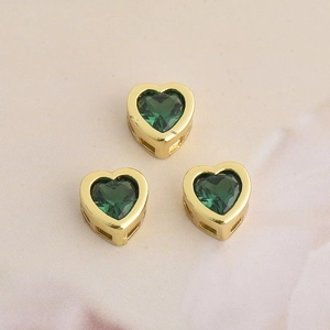 Detailed view of gold heart pendants with green zircon and hollow side designs