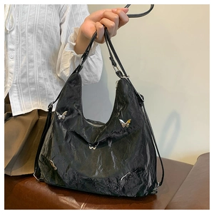 Close-up of black pleated tote bag featuring silver butterfly metal ornaments on soft texture