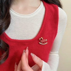 Close-up of a red enamel rocking horse brooch with zircon accents on a knit vest