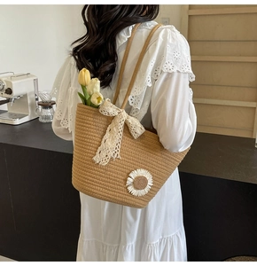Detail of straw woven tote with white daisy embroidery and lace bow on a white dress