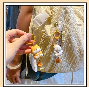 Detailed view of Shiba Inu and calico cat charms with bells on a beige backpack