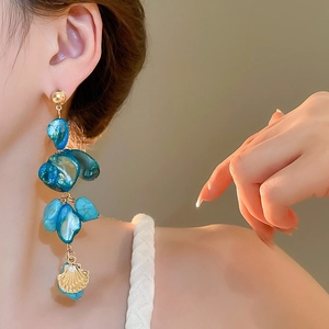 Close-up of blue shell earrings with a golden seashell pendant for beach vacations