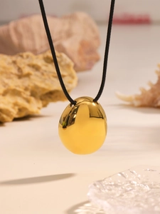 Macro detail of high-polish gold egg pendant necklace with sleek black cord on natural stone