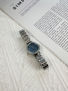 Detail of silver ladies watch with navy blue dial and rhinestone bezel on white fabric