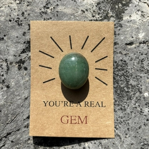 Close-up of green egg-shaped gemstone on kraft paper card with You're a Real Gem text