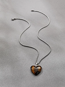 Macro shot of heart-shaped tiger eye stone pendant with silver twist chain on grey fabric