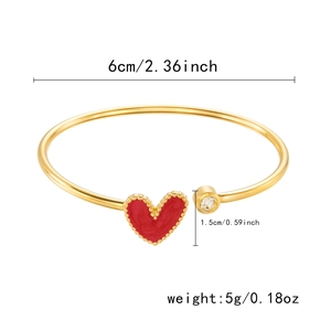 Detail showing the 6cm inner diameter and red heart charm of this gold open bangle