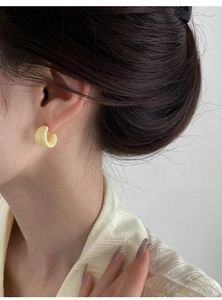 Detail view of a pale yellow C-shaped resin earring worn by a model in a minimalist style