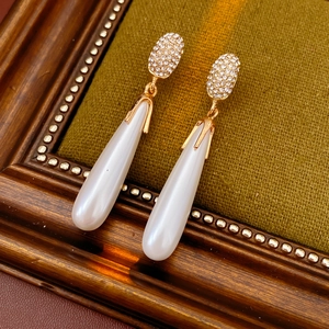 Close-up of golden teardrop pearl earrings with diamonds on green velvet background