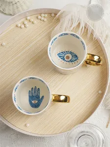 Detailed macro view of ceramic mugs featuring eye patterns and golden circle handles