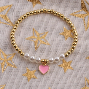 Close-up of golden beaded bracelet with white pearls and a pink heart pendant on fabric