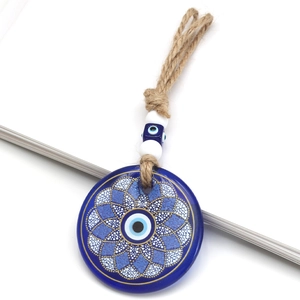 Macro shot of blue glass evil eye charm with gold floral mandala on white book