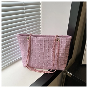 Pink textured tote bag with chain strap detail displayed by a sunlit window