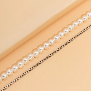 Detail of double-layer necklace with faux pearls and metal box chain on warm background
