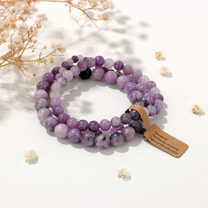 Close-up of three purple gemstone bead bracelets with tag on white textured surface