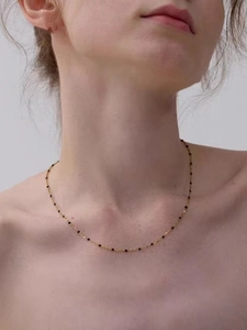 Close-up of minimalist gold chain necklace with small black beads on a woman's collarbone