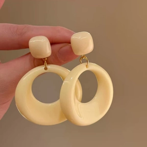 Detail of beige resin geometric hoop earrings held by hand against a brown wall