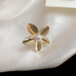Macro shot of a golden five-petal flower ring with a central pearl on silk fabric