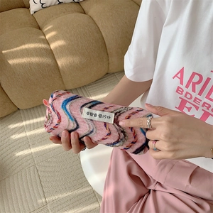 Détail d'une trousse de maquillage rose brodée arc-en-ciel tenue à la main.