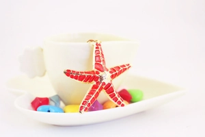Close-up of a red starfish keychain with gold trim hanging on a white cup edge