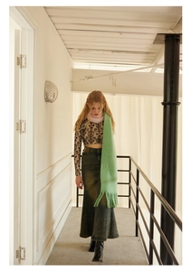 Detail of a green wool scarf with gradient fringes worn with a black crop top and denim skirt