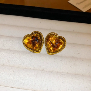 Close-up of amber heart-shaped resin earrings with detailed golden metal borders