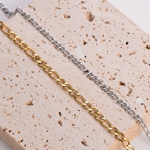 Close-up of gold and silver stainless steel Figaro chains on a stone display stand