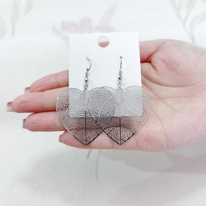 Macro detail of silver heart-shaped leaf earrings with delicate hollow-out vein patterns