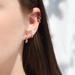 Elegant gold earrings set with zircon stones worn on ear for a layered jewelry look