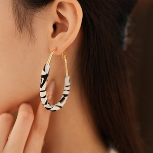 Gros plan sur la boucle d'oreille créole à motif zébré noir et blanc et fermoir doré