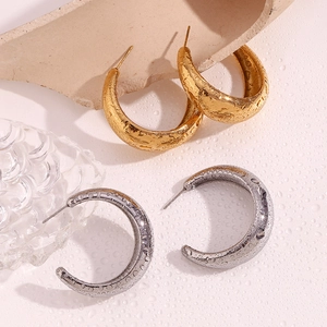 Macro shot of large polished C-shaped hoop earrings in gold and silver finish with water drops