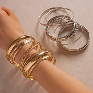 Detail of layered gold and silver metallic textured bangles set on a model's wrist